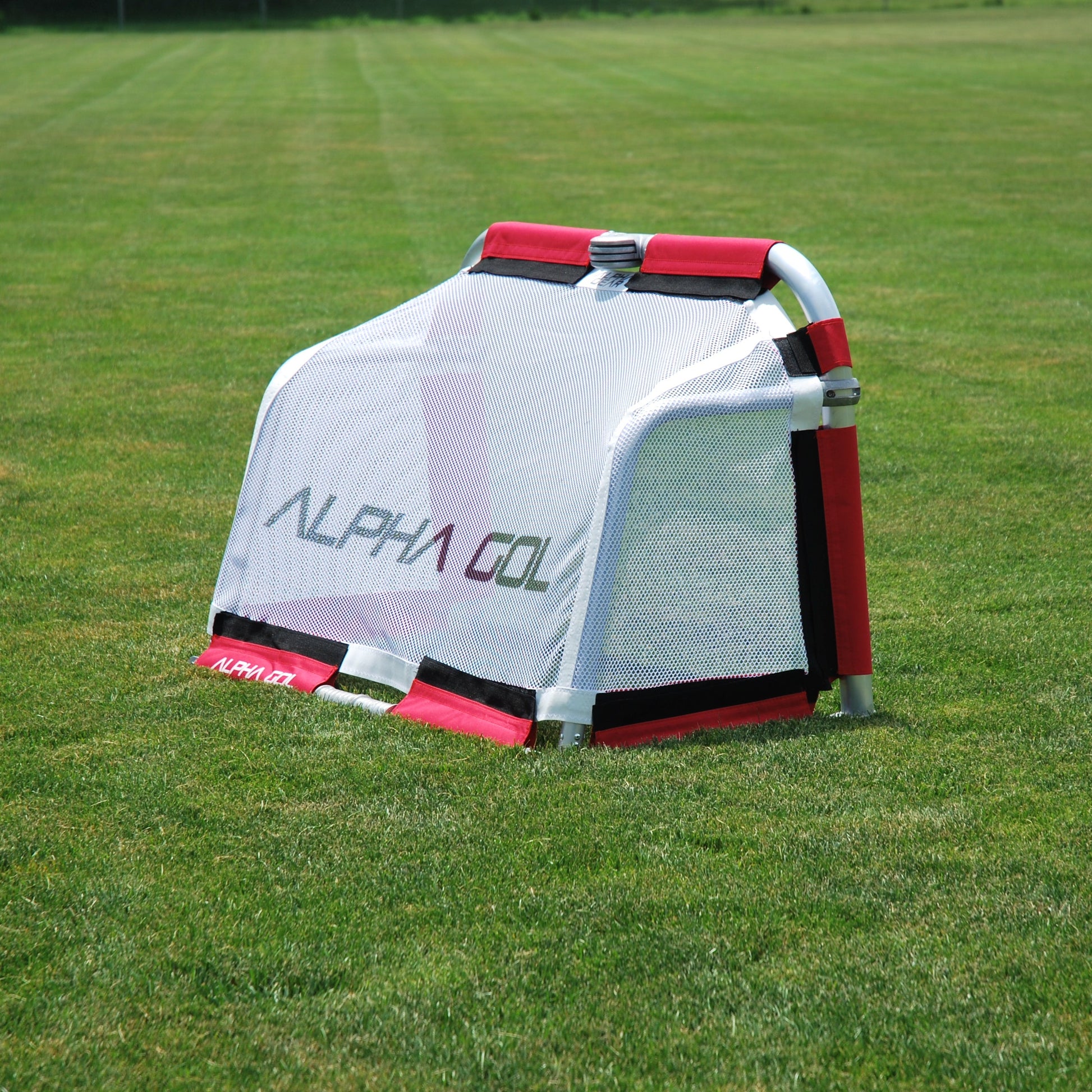 A portable golf target stand by Alpha Gol, featuring a white mesh body with red and black trim, set up on a green grass field.