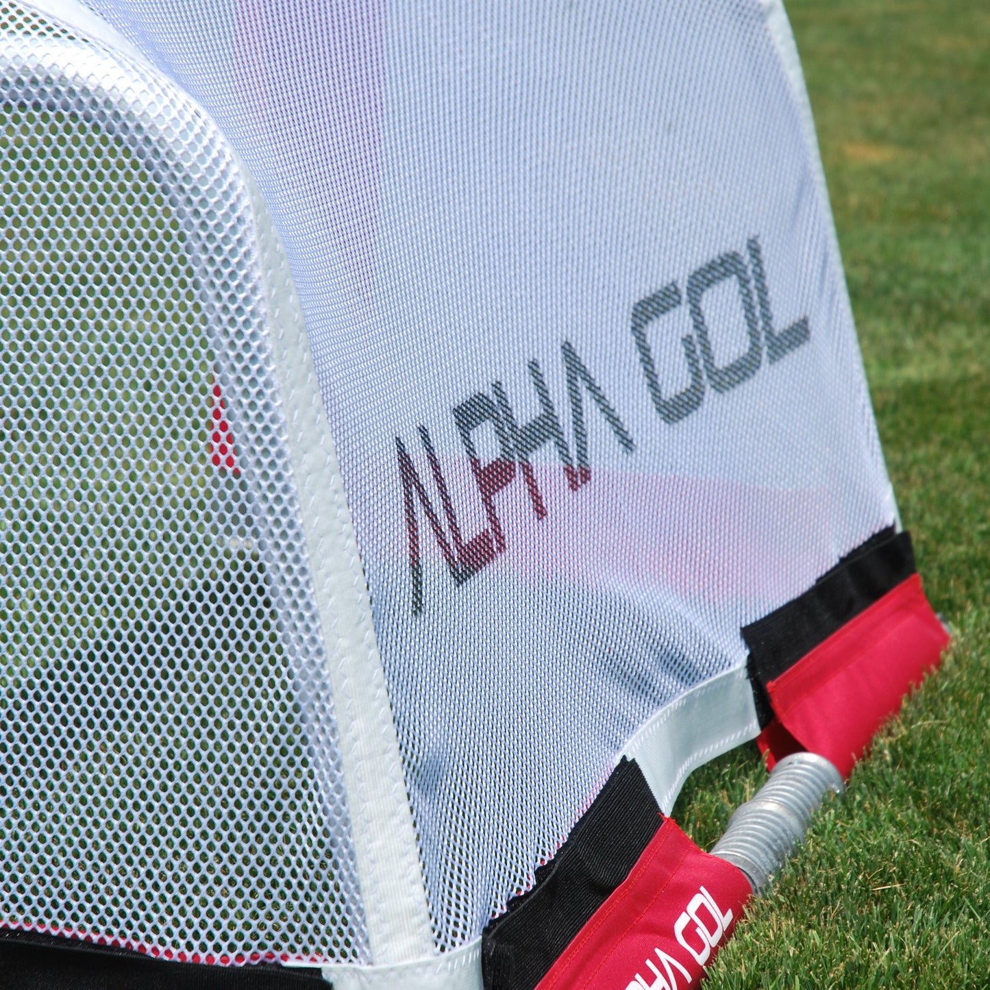 Close-up of a golf practice net on a grassy field, showing a white mesh back wall with the brand name ALPHA GOL printed in gray and red trim.